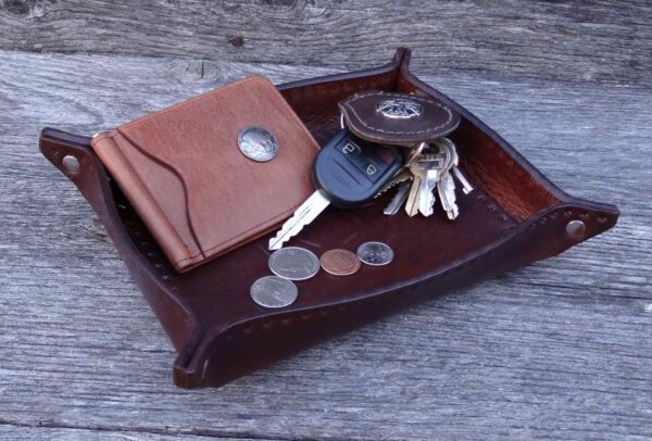 A brown leather tray with keys, wallet and coins.