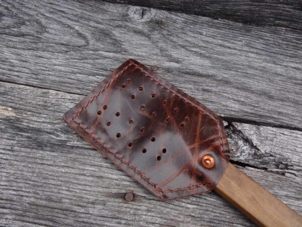 A wooden spatula with holes in it laying on top of a table.