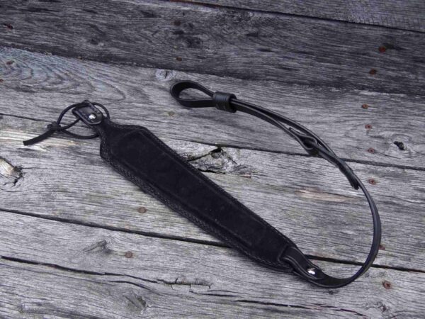 A black leather strap laying on top of a wooden surface.