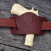A gun is laying on the ground with a leather holster.