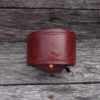A red leather cuff bracelet on top of a wooden surface.