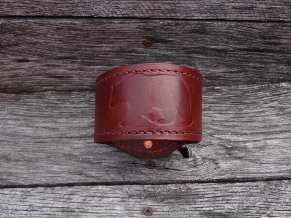 A red leather cuff bracelet on top of a wooden surface.