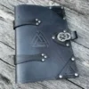 A black leather book with metal rivets and a triangular symbol.