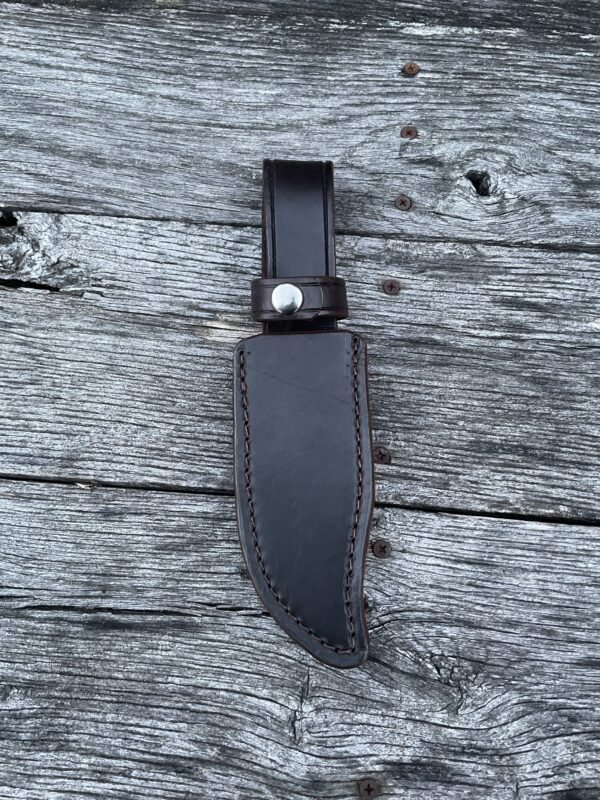 A black knife with a leather sheath on top of it.