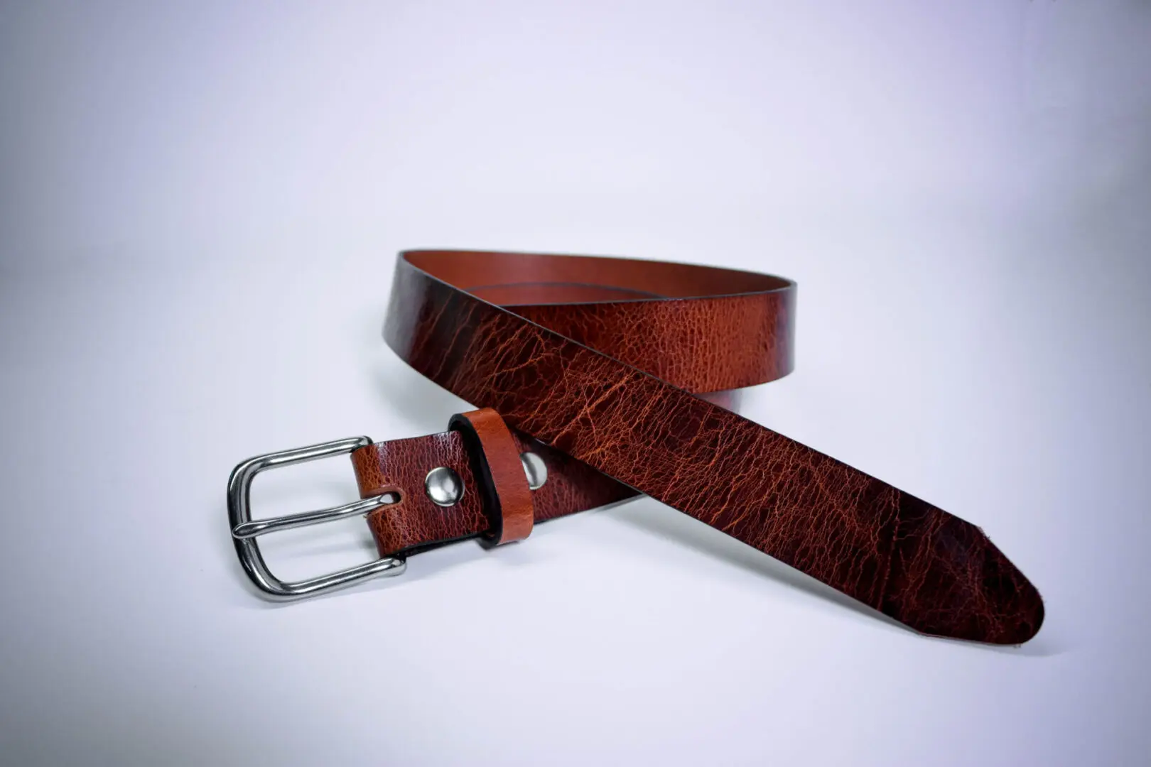 A brown leather belt with silver buckle on top of white surface.